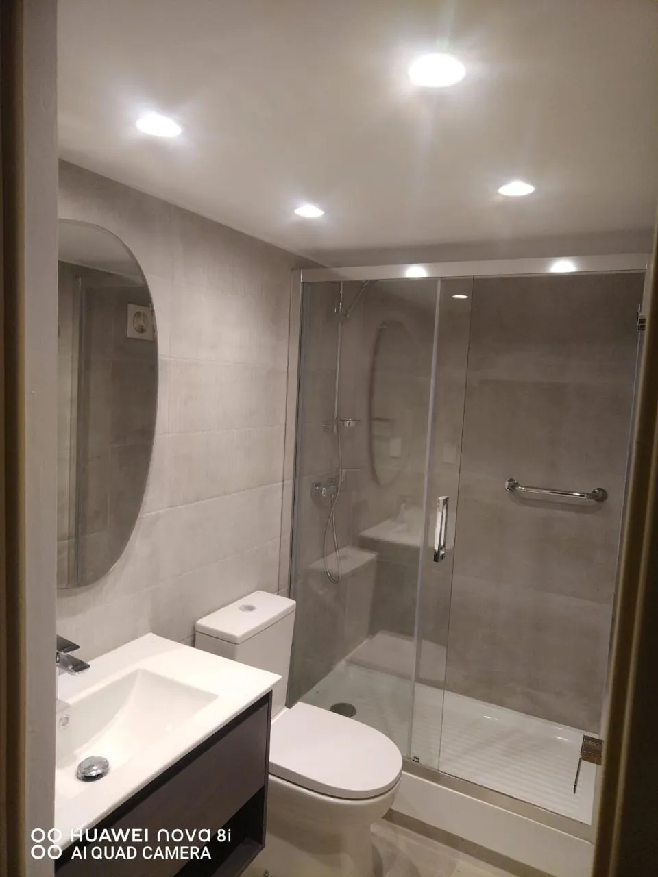 Baño completo con ducha de vidrio corredera, espejo ovalado y porcelanato beige
