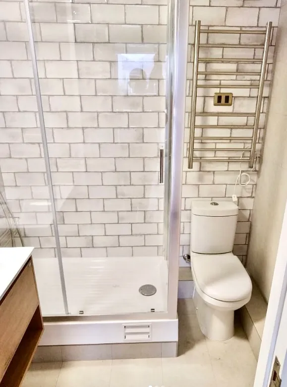 Baño con cerámica tipo metro blanca, receptáculo de ducha y toallero eléctrico