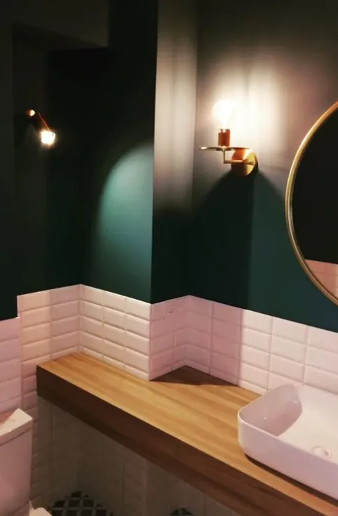Baño con muro verde, cerámica biselada blanca y cubierta de madera