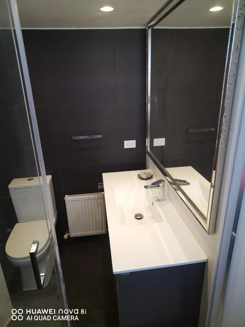 Baño con porcelanato negro de gran formato, vanitorio blanco y espejo enmarcado