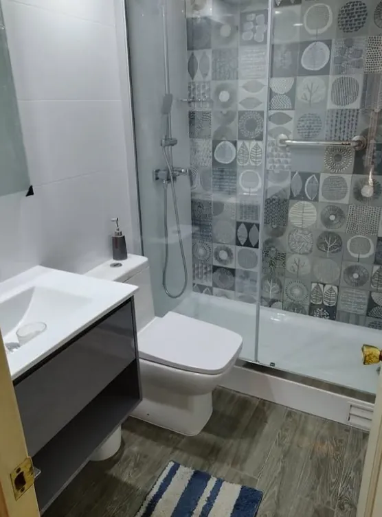 Baño remodelado con ducha de vidrio, vanitorio gris y piso símil madera