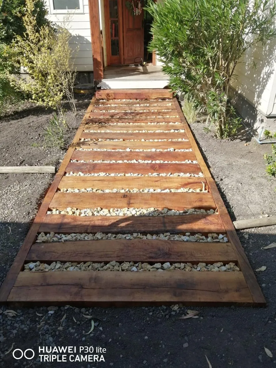 Pasarela exterior de madera con gravilla blanca hacia la entrada de una casa